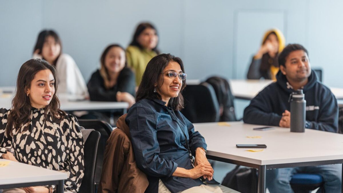 Preethi sits at a desk surrounded by other students