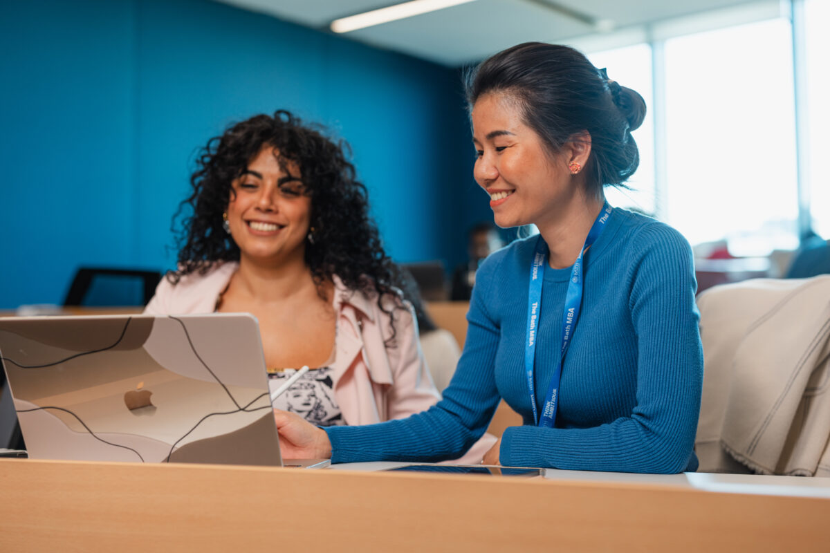 Two MBA students looking at a laptop and smiling